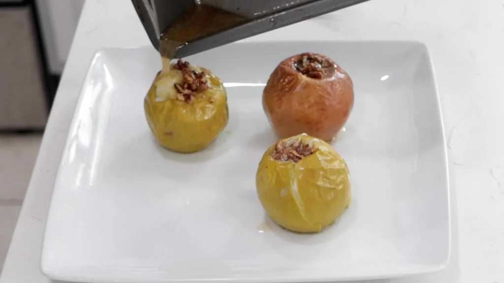 Pouring juice over freshly baked apples on a white plate.