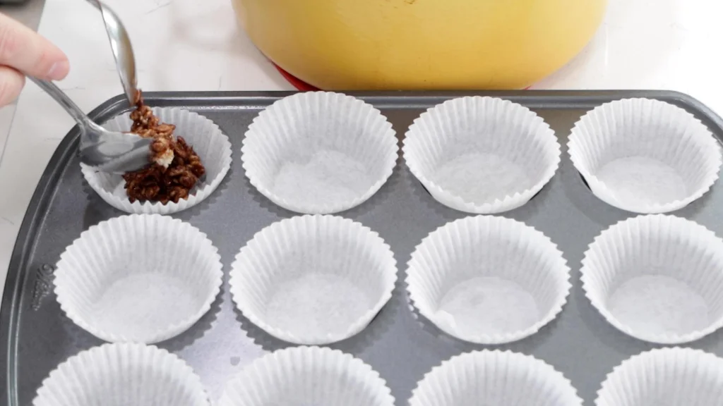 Two spoons scooping mixture into a muffin cup.