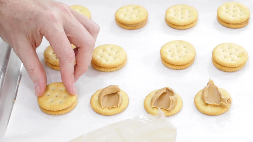 Hand pressing a Ritz cracker on top of some peanut butter.