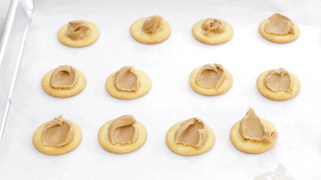 Ritz crackers with peanut butter in the middle of them on a sheet pan lined with parchment paper.