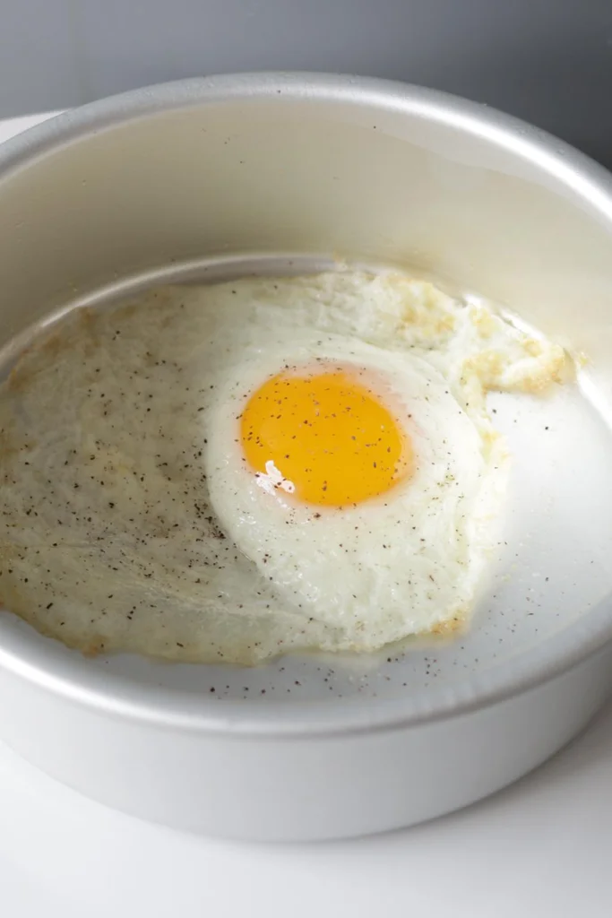 Fried egg in a cake pan on a white plate.
