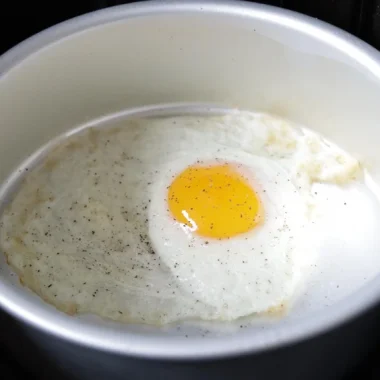 Fried egg in cake pan in an air fryer basket.