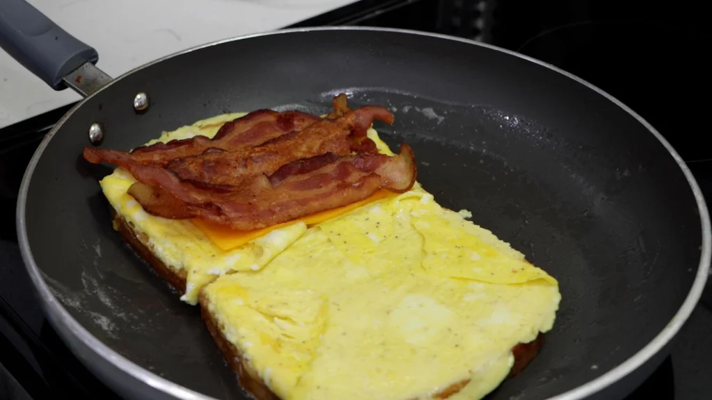 Three slices of cooked bacon and a slice of cheese on an egg sandwich