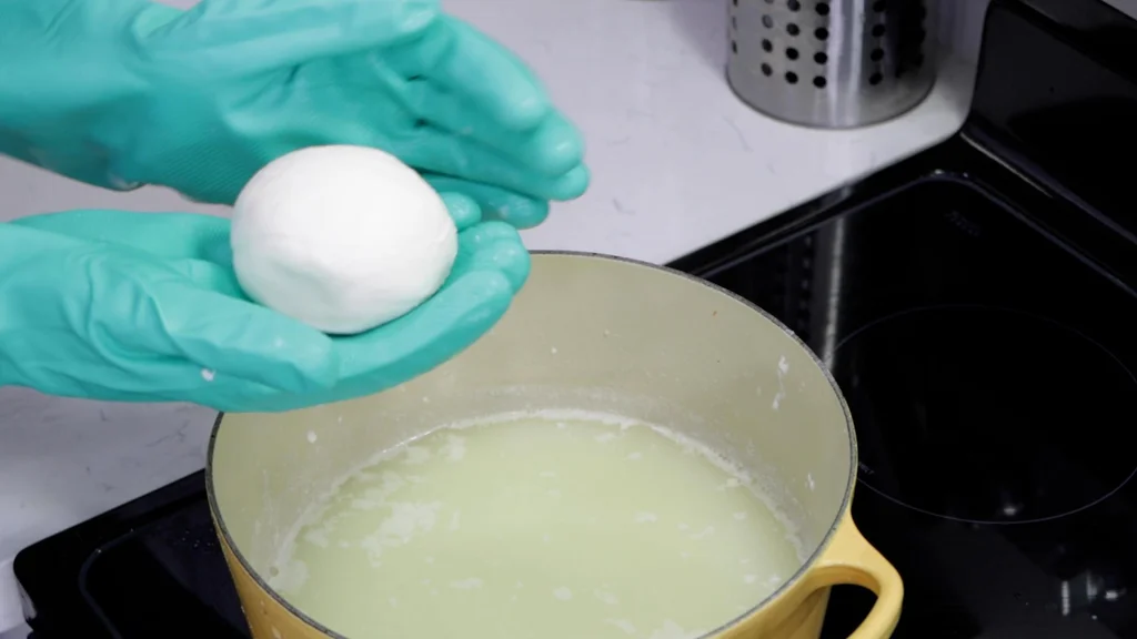 Hand forming a mozzarella cheese ball.