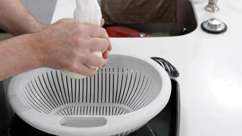 Hands squeezing the whey out of mozzarella curds.