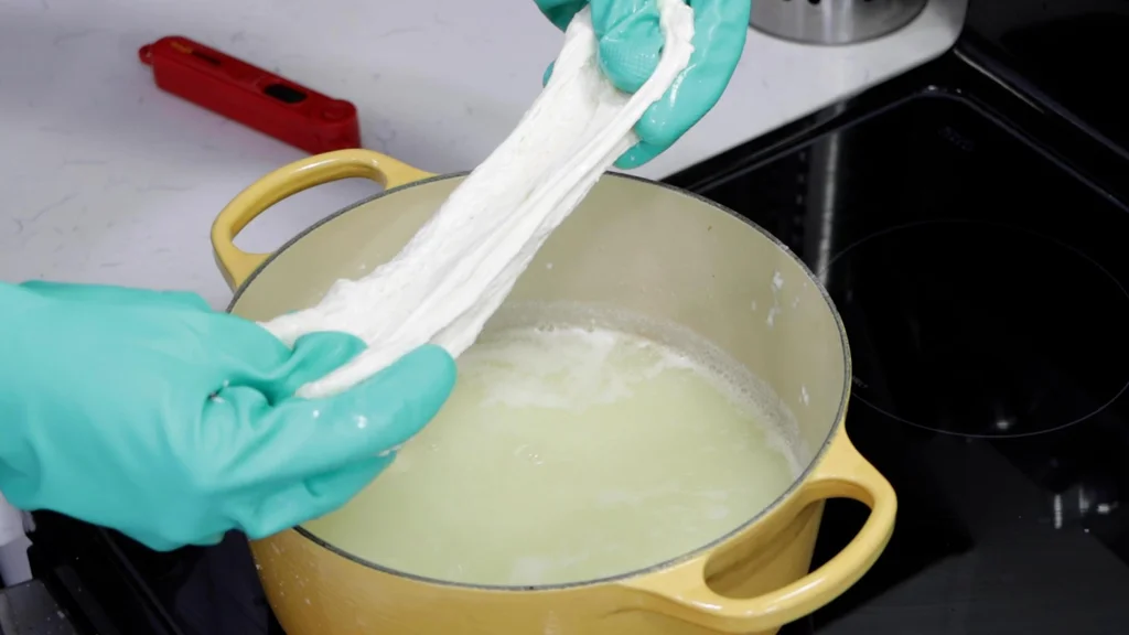 Hands stretching homemade mozzarella cheese.