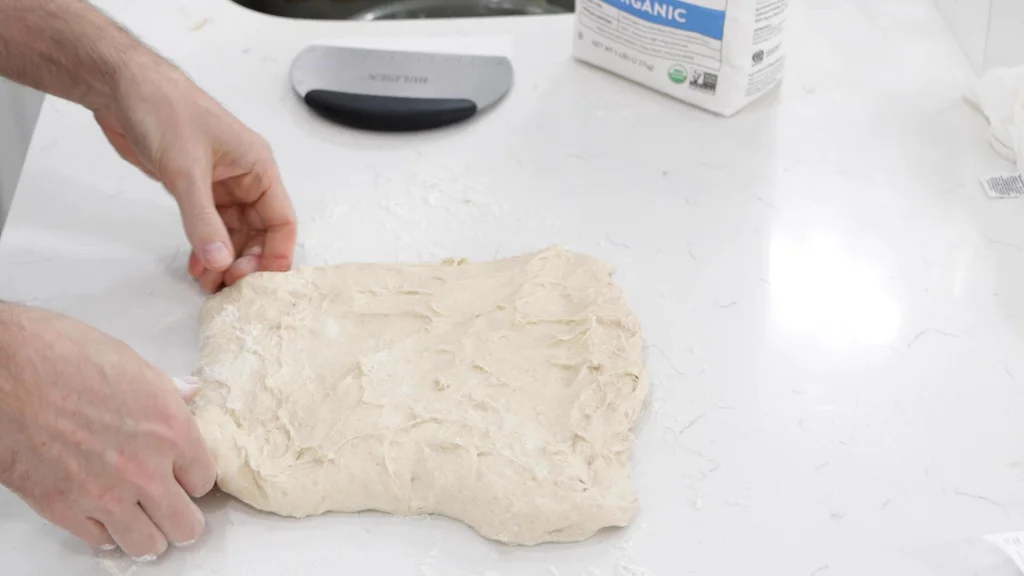 Fingers stretching dough into a rectangle.