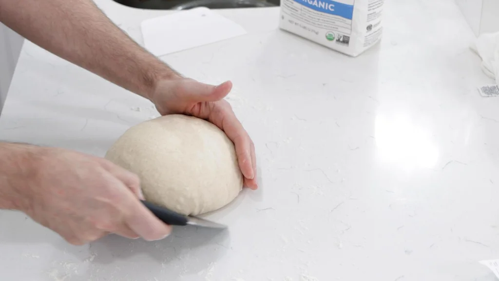 Hand scraping the dough and pulling it towards him creating tension.