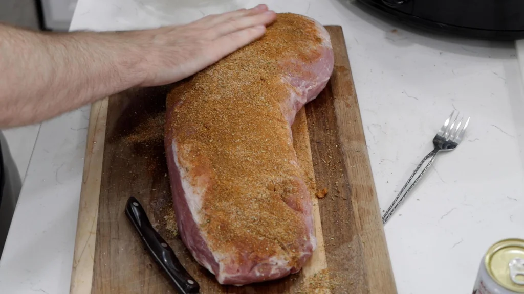 Hand patting a pork loin with a dry rub.