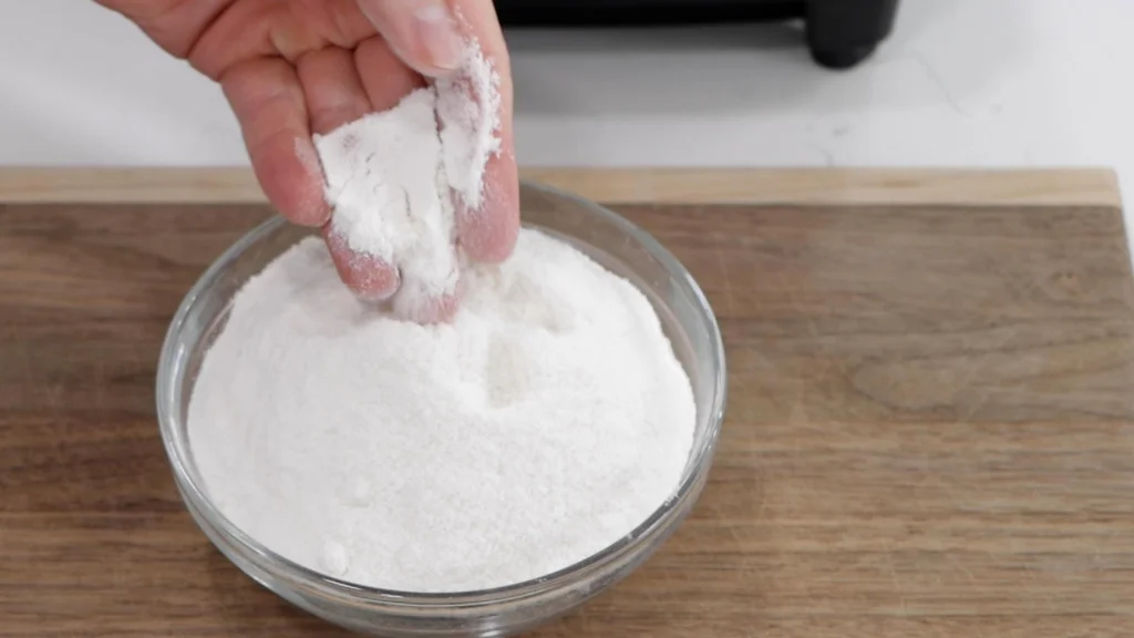 Fingers holding rice flour in a bowl.