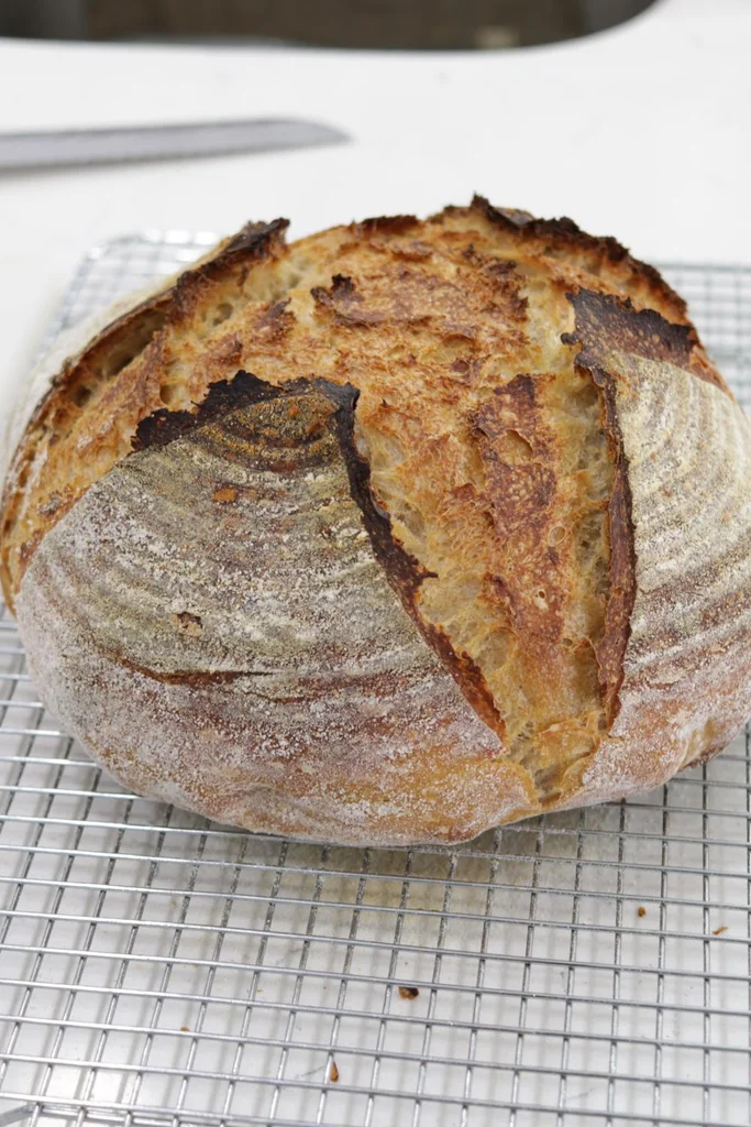 Loaf of sourdough bread cooling on a wire rack.