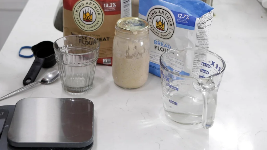 Flour, water, sourdough starter, and a scale on a counter.