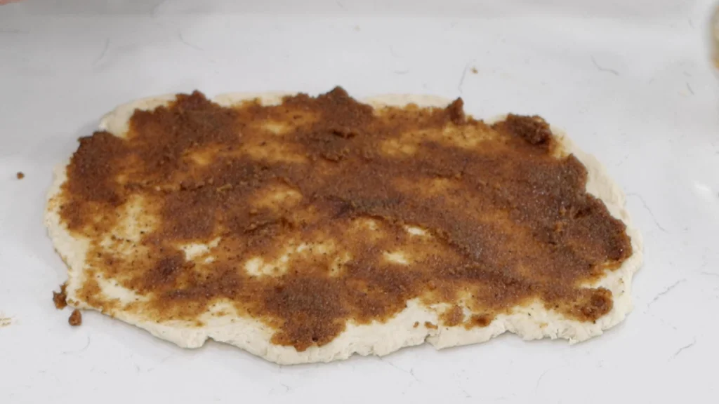 Cinnamon rolls dough rolled out flat with filling spread evenly on top.