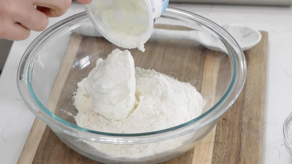 Hand dumping yogurt into a bowl with self-rising flour.