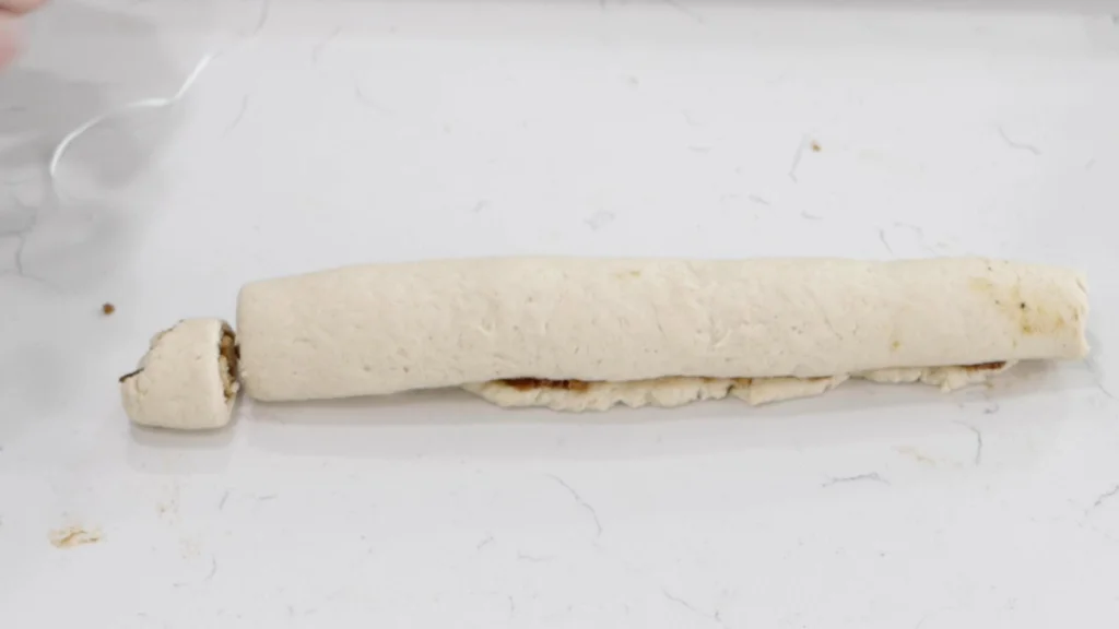 Cut cinnamon roll next to a log-shaped rolled up dough.