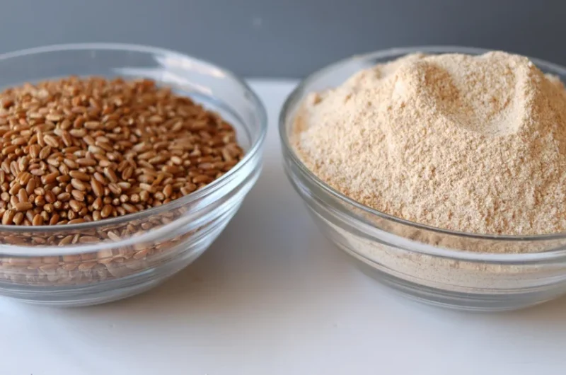A bowl of wheat berries next to a bowl of freshly ground flour.
