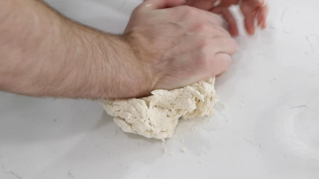 Hand kneading cinnamon roll dough on a counter.