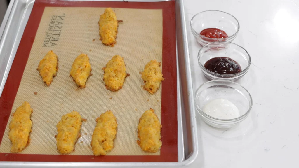 Freshly baked homemade chicken fingers on a sheet pan lined with a silicone baking mat.