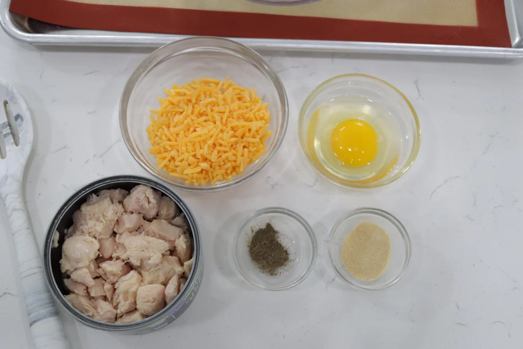 Canned chicken, cheese, and a few other ingredients on a white countertop.