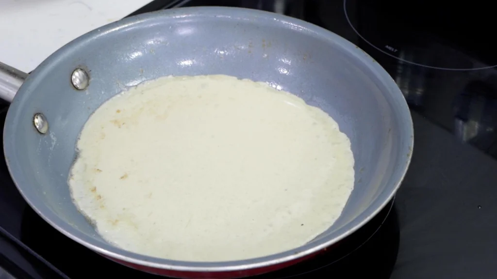 Cooking the crepe in a nonstick skillet on a stovetop burner.