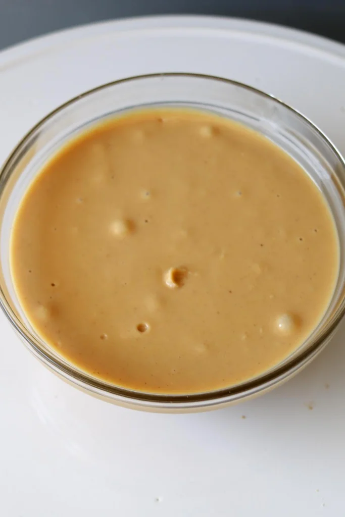 A glass bowl full of creamy homemade peanut butter. 