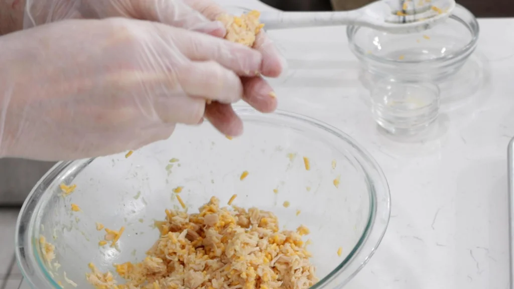 Hands with gloves forming the chicken mixture into finger shapes.