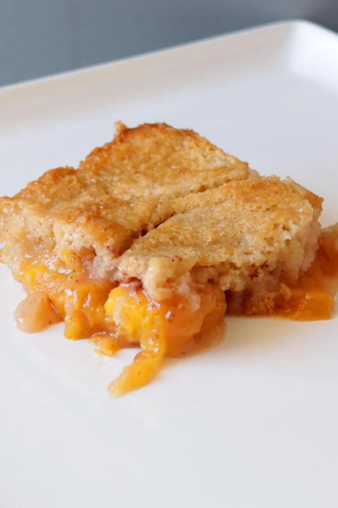 Slice of homemade peach cobbler on a white plate.
