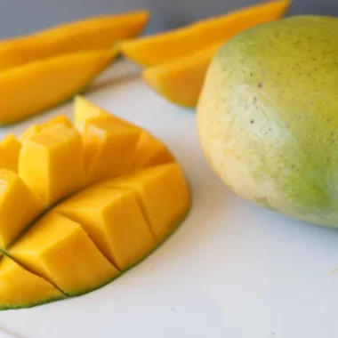 sliced mango next to a whole mango on a white plate.