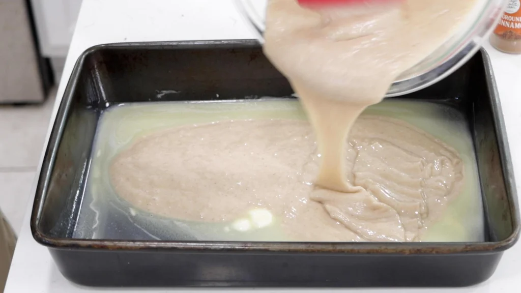 Batter being poured over the top of melted butter in a baking pan.