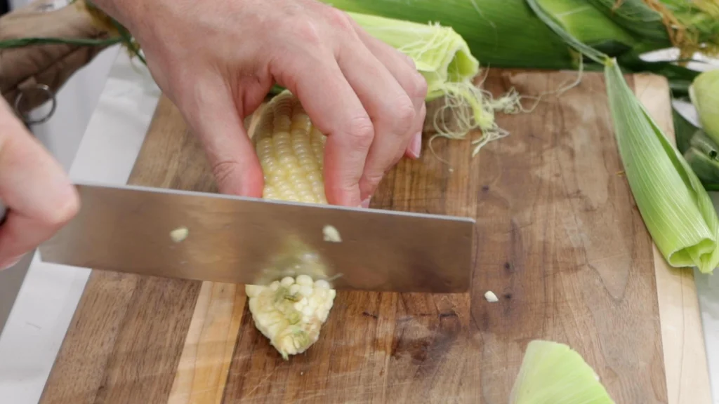 Knife slicing the stalk end of the corn off.
