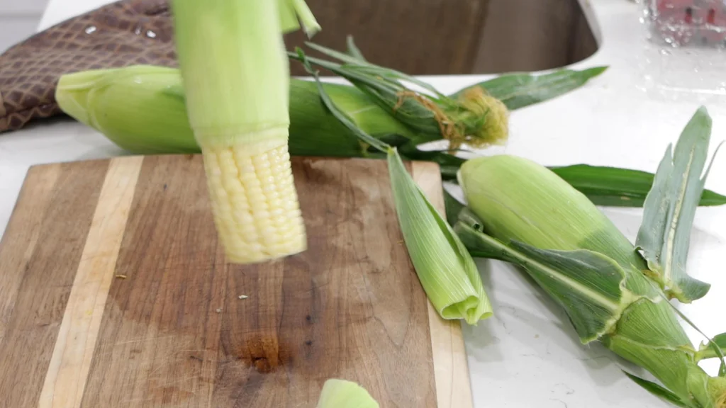 Hand wiggling and ear of corn so the corn can slide out of the husk.