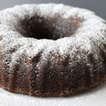 Oreo bundt cake on a white cake pedestal topped with powdered sugar.