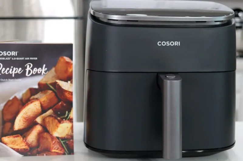 Cosori air fryer on a counter next to a recipe book