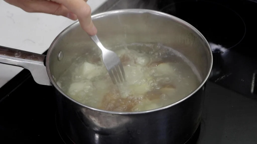 Fork poking potato chunks in boiling water. Fork poking potato chunks in boiling water.