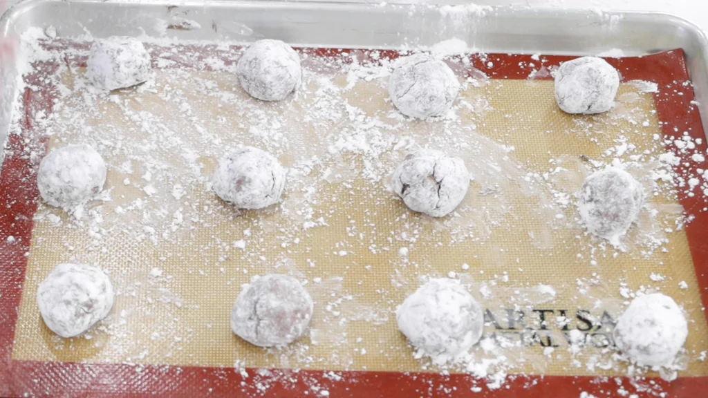 Balls of Cool Whip cookie dough rolled in powdered sugar on a sheet pan lined with a silicone baking mat. Balls of Cool Whip cookie dough rolled in powdered sugar on a sheet pan lined with a silicone baking mat.
