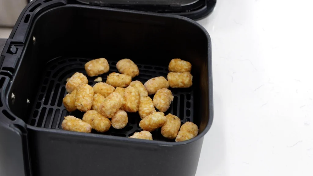 several frozen tater tots in an air fryer basket. several frozen tater tots in an air fryer basket.