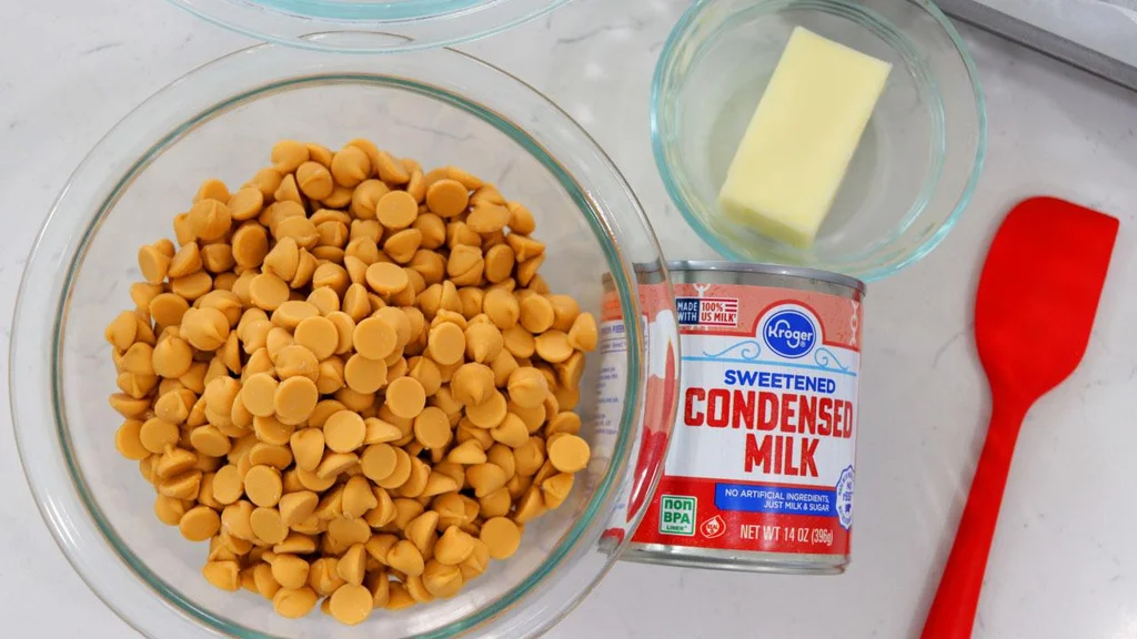 butterscotch chips, sweetened condensed milk, and butter on top of a white countertop. butterscotch chips, sweetened condensed milk, and butter on top of a white countertop.