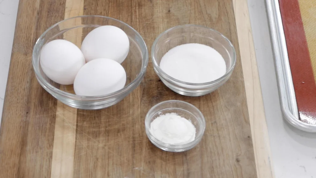 Eggs, sugar, and cornstarch in glass bowls on a wooden cutting board. Eggs, sugar, and cornstarch in glass bowls on a wooden cutting board.