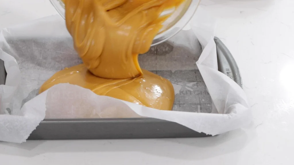 Pouring hot butterscotch fudge into a pan lined with parchment paper. Pouring hot butterscotch fudge into a pan lined with parchment paper.
