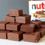 Pile of Nutella fudge squares on a white plate next to a container of Nutella.