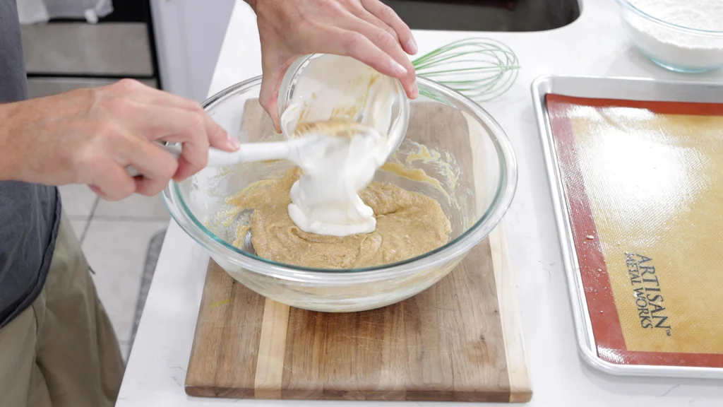 Hand scooping cottage cheese into a bowl of cookie dough. Hand scooping cottage cheese into a bowl of cookie dough.