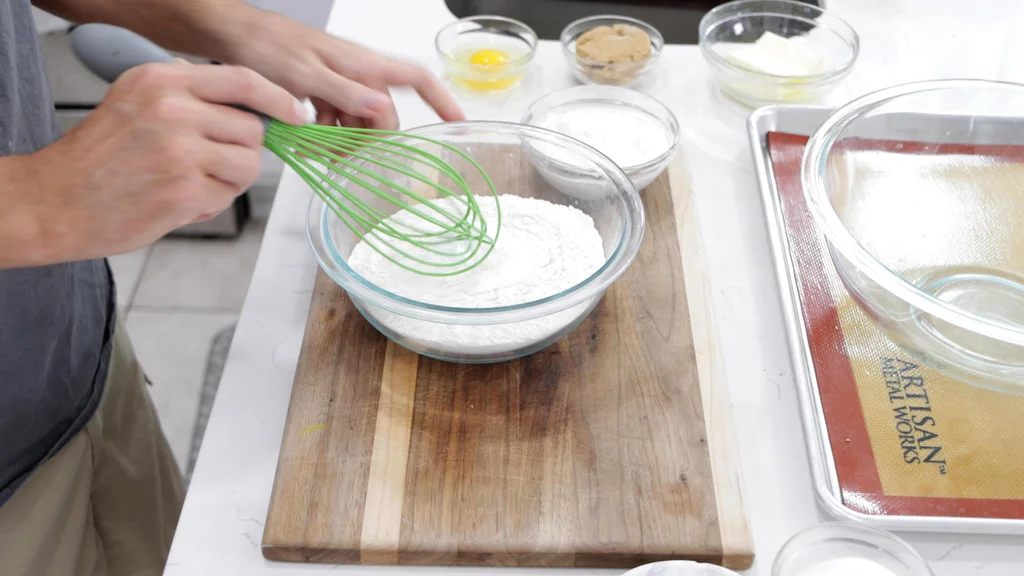 hand whisking flour, salt, and baking soda in a medium glass bowl. hand whisking flour, salt, and baking soda in a medium glass bowl.
