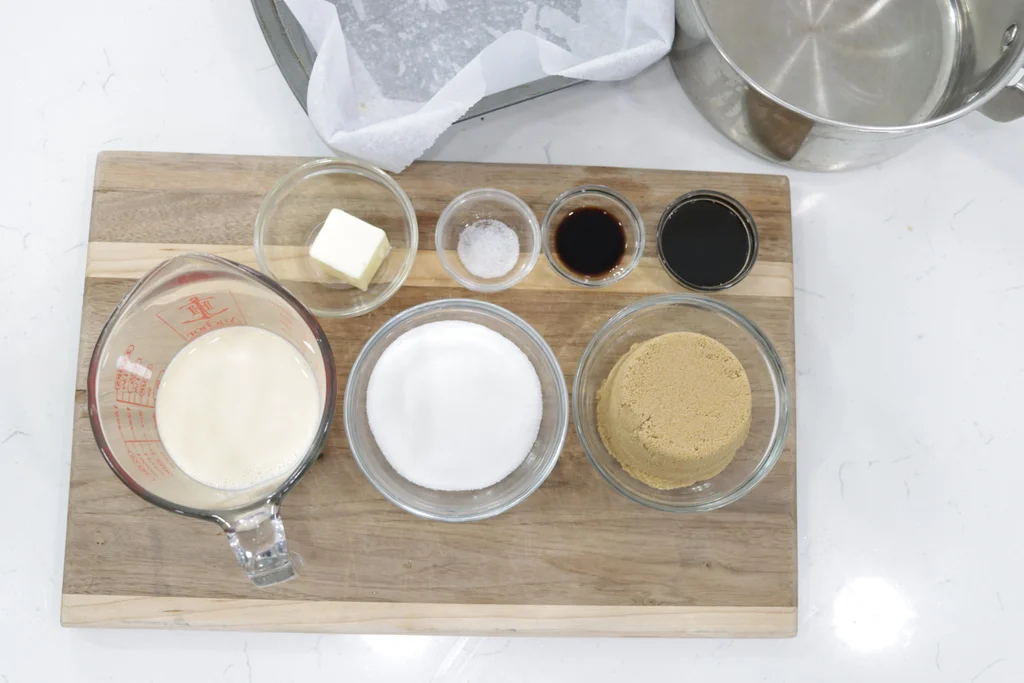 evaporated milk, sugar, butter and a few other ingredients in glass bowls on top of a wooden cutting board. evaporated milk, sugar, butter and a few other ingredients in glass bowls on top of a wooden cutting board.