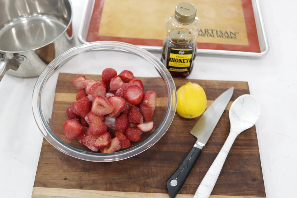 Bowl of frozen strawberries next to a lemon and honey on a wooden cutting board. Bowl of frozen strawberries next to a lemon and honey on a wooden cutting board.