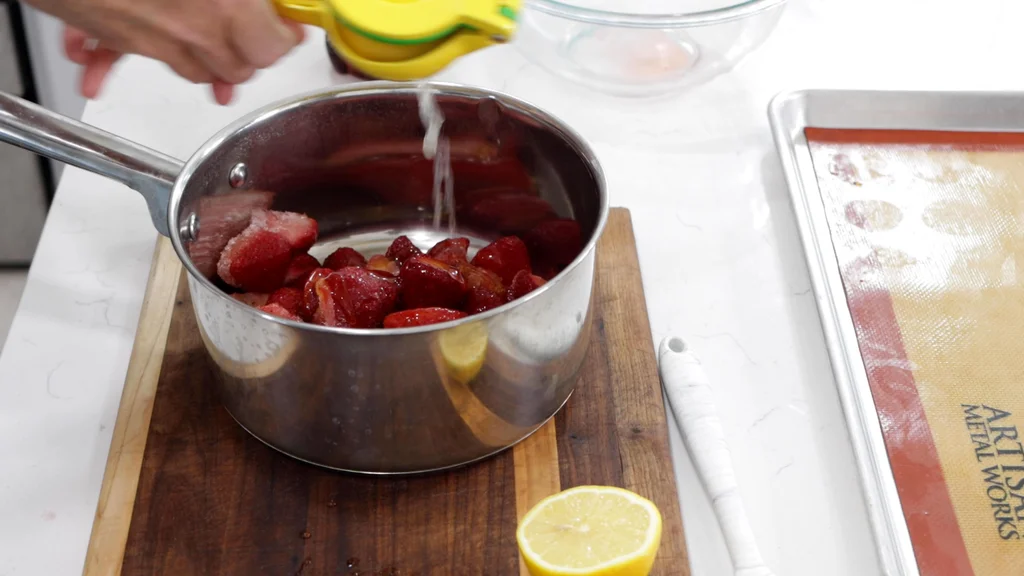 Hand squeezing lemon juice into a pot with strawberries and honey. Hand squeezing lemon juice into a pot with strawberries and honey.