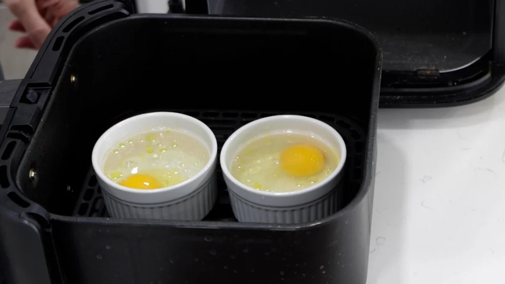 Two ramekins with eggs resting in the basket of an air fryer. Two ramekins with eggs resting in the basket of an air fryer.