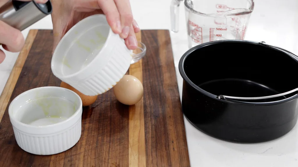 Hand spraying olive oil into white ramekins. Hand spraying olive oil into white ramekins.