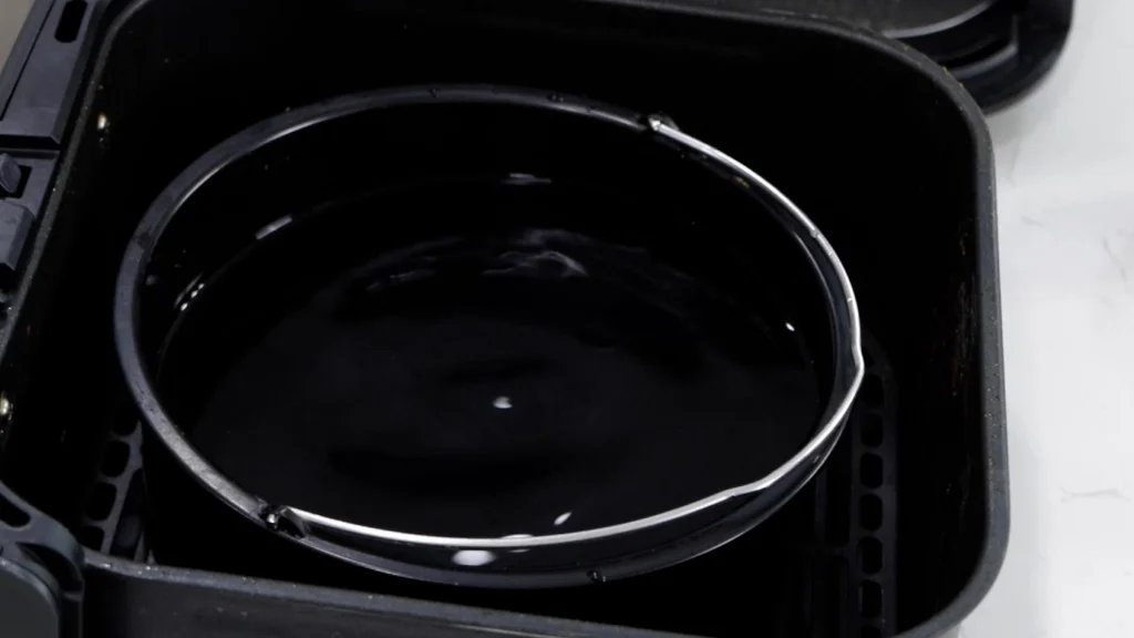Pot filled with water in an air fryer basket. Pot filled with water in an air fryer basket.