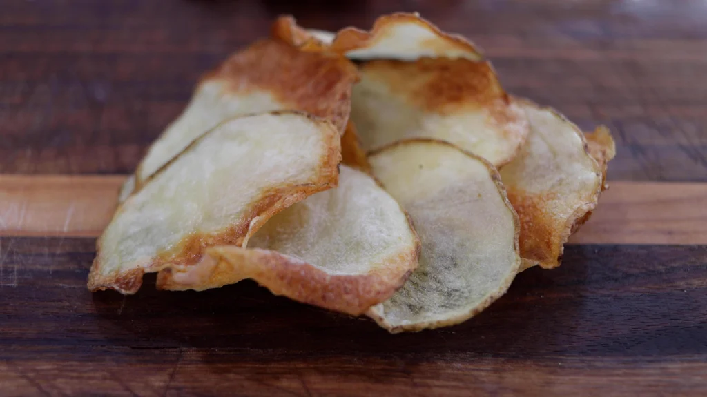 Finished air fryer potato chips piled on a wooden cutting board. Finished air fryer potato chips piled on a wooden cutting board.