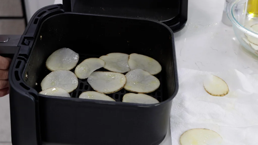 Several potato slices arranged on the bottom of an air fryer basket. Several potato slices arranged on the bottom of an air fryer basket.